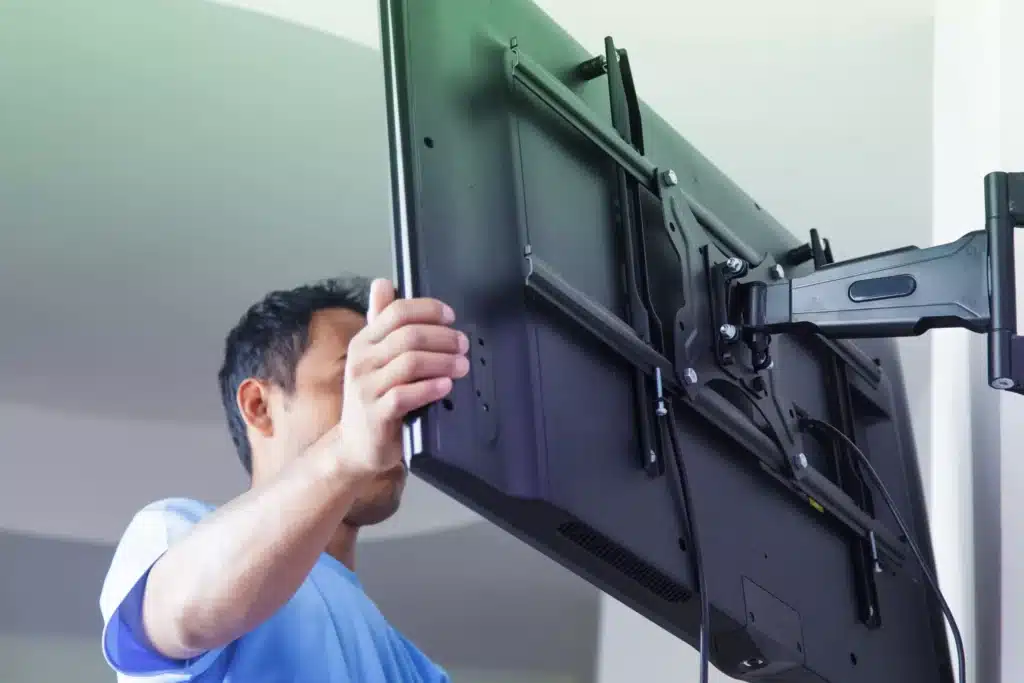 Un homme installe une télévision sur un support mural orientable articulé